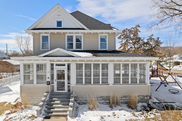 view of front facade with a sunroom, roof with shingles, and fence