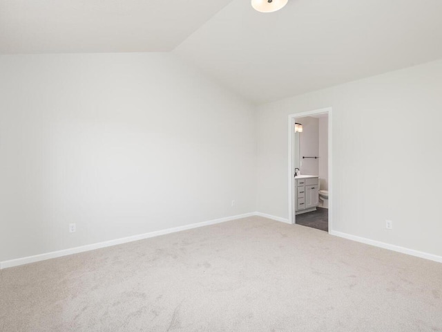 unfurnished bedroom with vaulted ceiling, dark colored carpet, ensuite bath, and baseboards