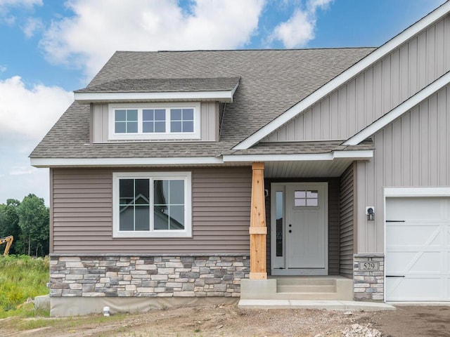 view of front of house with a garage, stone siding, and roof with shingles