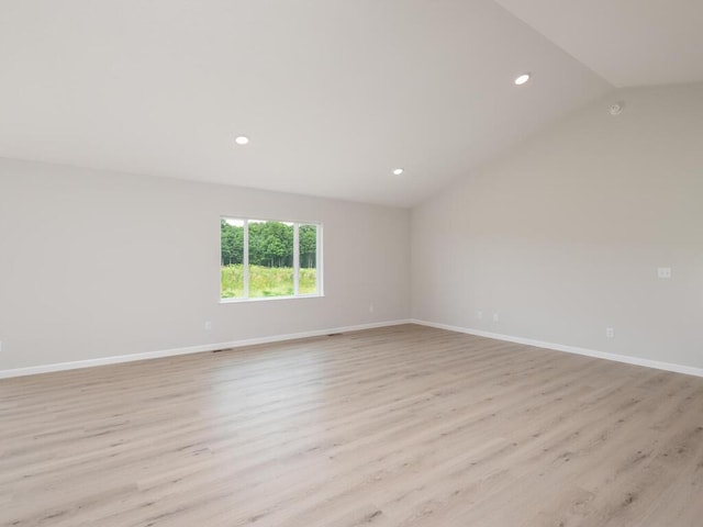 spare room with vaulted ceiling, light wood-type flooring, and baseboards