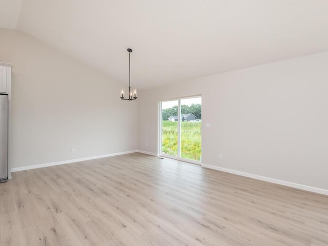 spare room featuring a chandelier, light wood finished floors, lofted ceiling, and baseboards