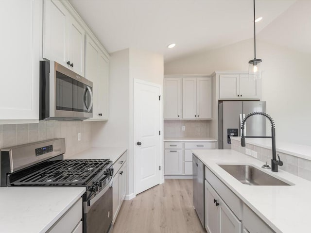 kitchen with lofted ceiling, appliances with stainless steel finishes, white cabinets, and a sink