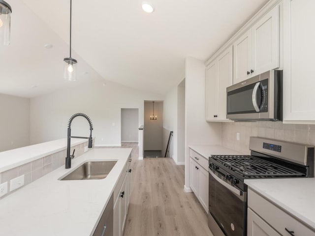 kitchen featuring decorative backsplash, appliances with stainless steel finishes, vaulted ceiling, light wood-type flooring, and a sink