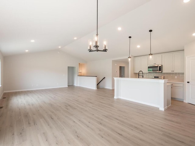 kitchen with stainless steel microwave, backsplash, vaulted ceiling, light wood-style floors, and a sink