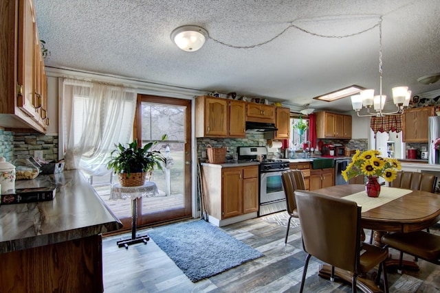 kitchen featuring under cabinet range hood, a textured ceiling, stainless steel gas range oven, and tasteful backsplash