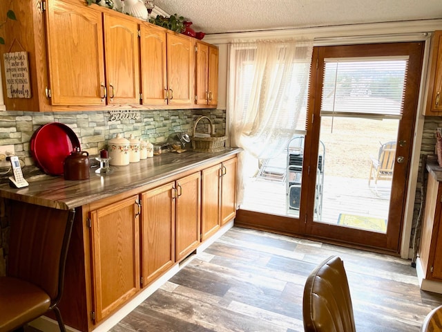 interior space with light wood-style flooring, a textured ceiling, brown cabinets, and tasteful backsplash