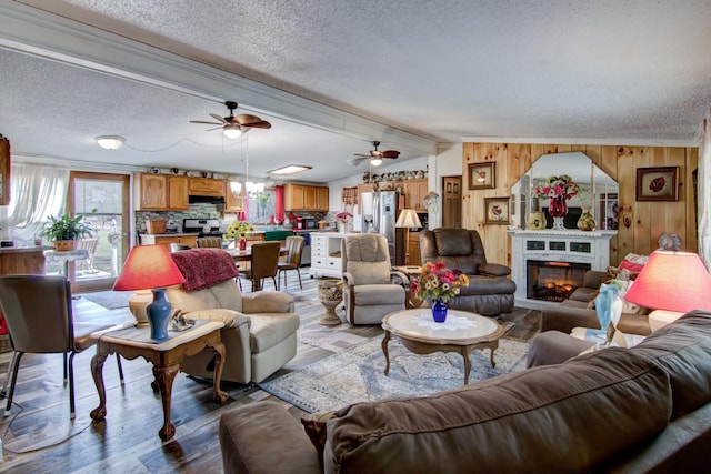 living room featuring wood walls, wood finished floors, a glass covered fireplace, a textured ceiling, and ceiling fan