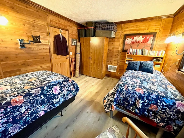 bedroom featuring wooden walls, wood finished floors, visible vents, crown molding, and a textured ceiling