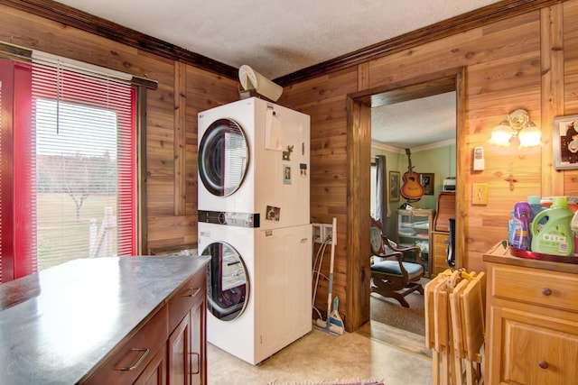 clothes washing area featuring a textured ceiling, stacked washer / dryer, wood walls, laundry area, and ornamental molding