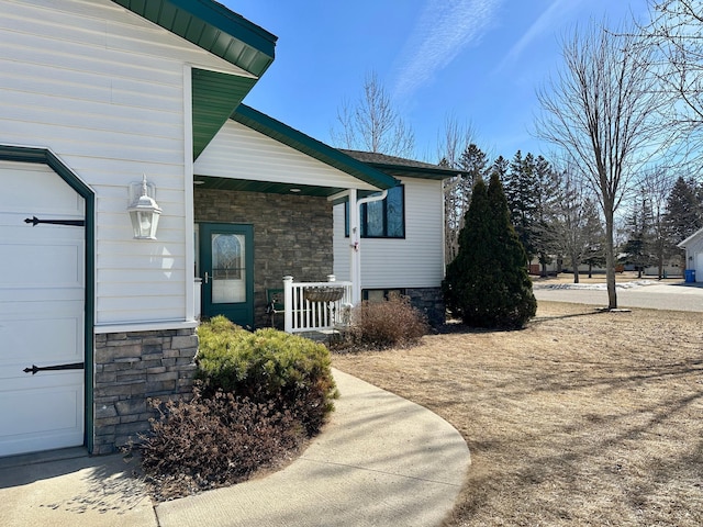 view of side of home featuring stone siding, covered porch, and an attached garage