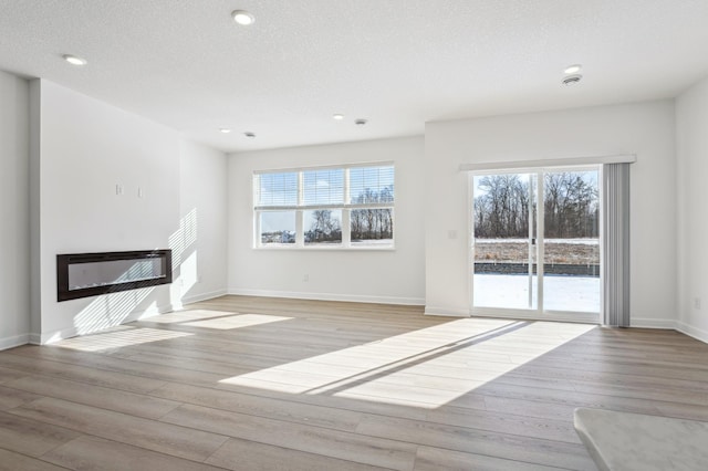 unfurnished living room with light wood-style floors, plenty of natural light, a textured ceiling, and a glass covered fireplace