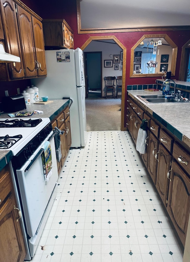 kitchen with arched walkways, range hood, freestanding refrigerator, a sink, and gas range