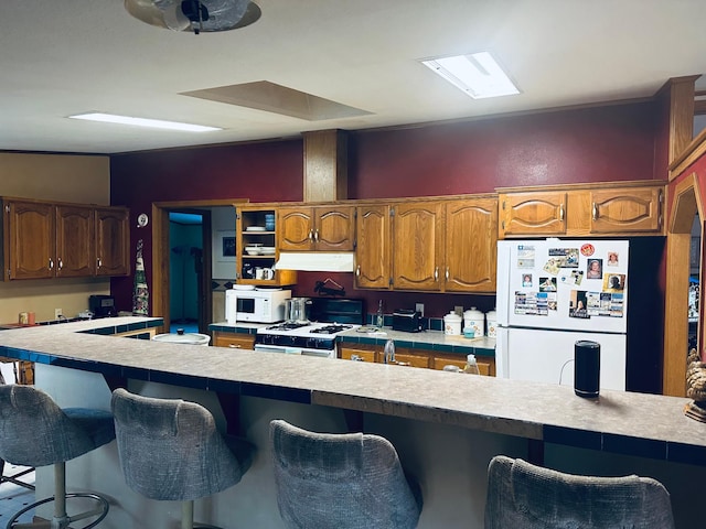 kitchen with light countertops, white appliances, a breakfast bar, and under cabinet range hood