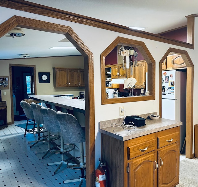 bar with lofted ceiling, under cabinet range hood, freestanding refrigerator, and crown molding