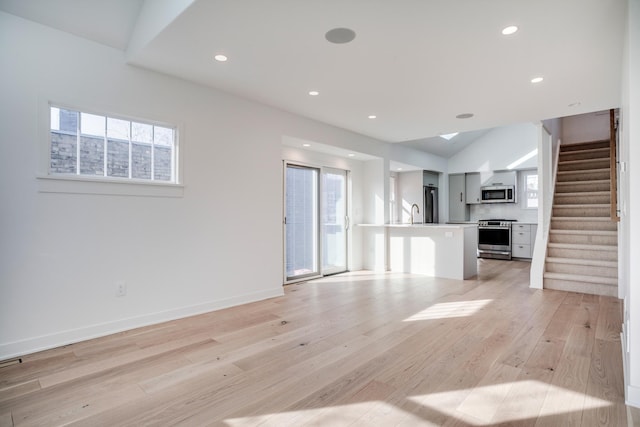 unfurnished living room with stairs, a wealth of natural light, recessed lighting, and light wood finished floors