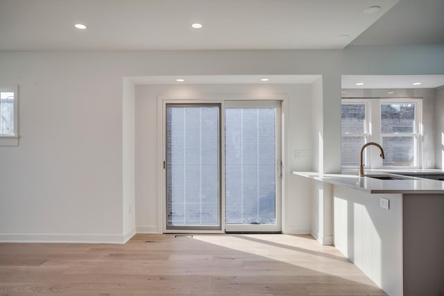 kitchen featuring baseboards, recessed lighting, light wood-style flooring, white cabinets, and a sink