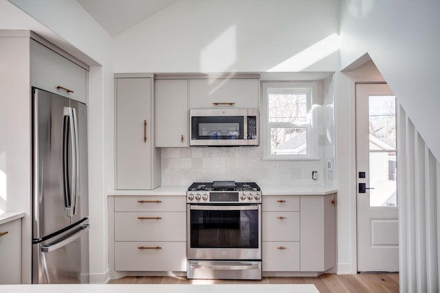 kitchen with lofted ceiling, gray cabinetry, light countertops, appliances with stainless steel finishes, and backsplash