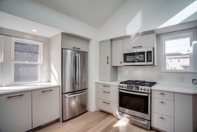 kitchen featuring gray cabinetry, stainless steel appliances, light countertops, decorative backsplash, and lofted ceiling