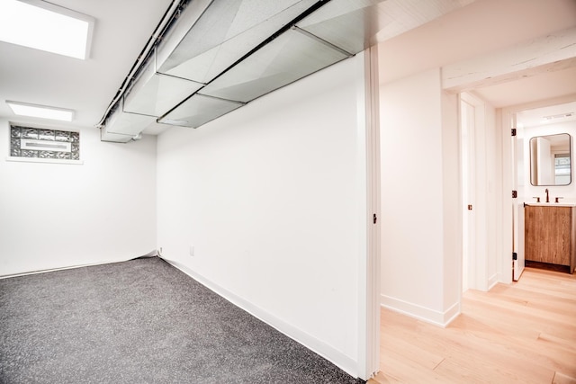 finished below grade area featuring a sink, baseboards, and light wood-style floors