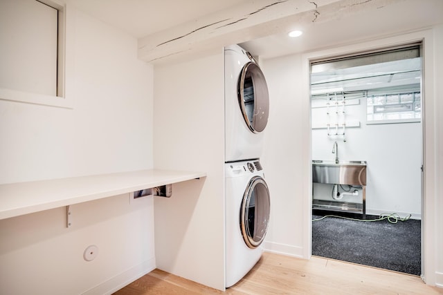 laundry room with baseboards, laundry area, a sink, light wood-style floors, and stacked washer / drying machine