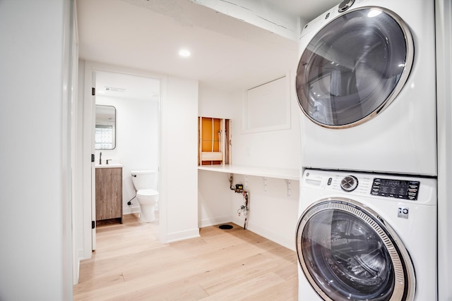 laundry room featuring light wood-type flooring, stacked washer / drying machine, baseboards, and laundry area