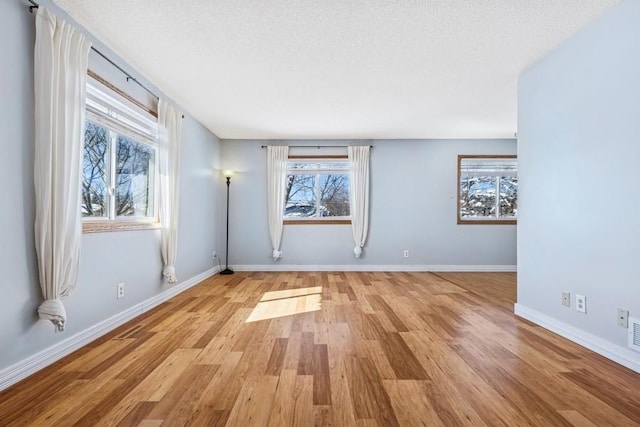 empty room with visible vents, a textured ceiling, baseboards, and wood finished floors