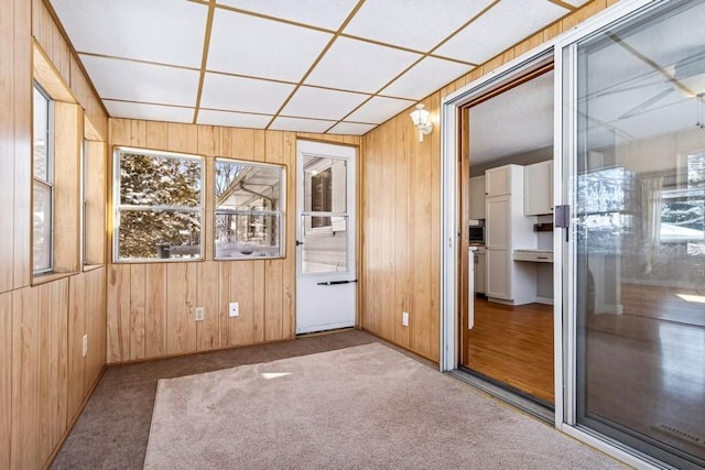 carpeted spare room with a paneled ceiling and wood walls