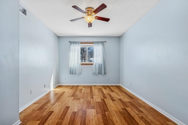 empty room featuring visible vents, a textured ceiling, baseboards, and wood finished floors