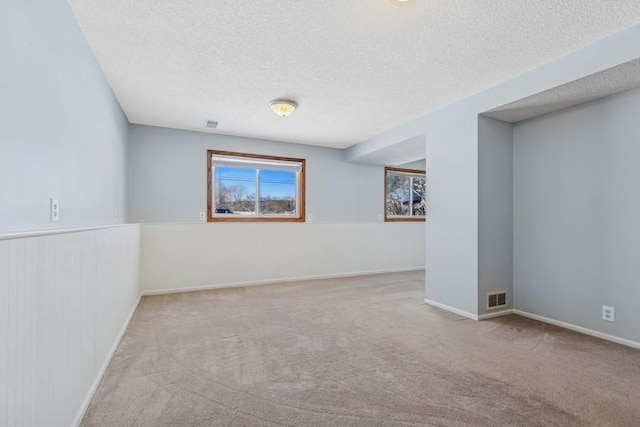 carpeted empty room with visible vents, a textured ceiling, and baseboards