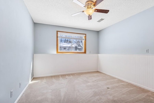 carpeted spare room with a ceiling fan, visible vents, a textured ceiling, and wainscoting