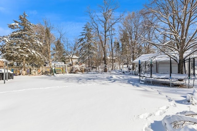 yard layered in snow featuring a trampoline, fence, and a detached garage