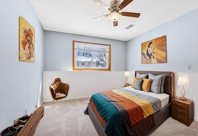 bedroom with light carpet, a textured ceiling, visible vents, and a ceiling fan