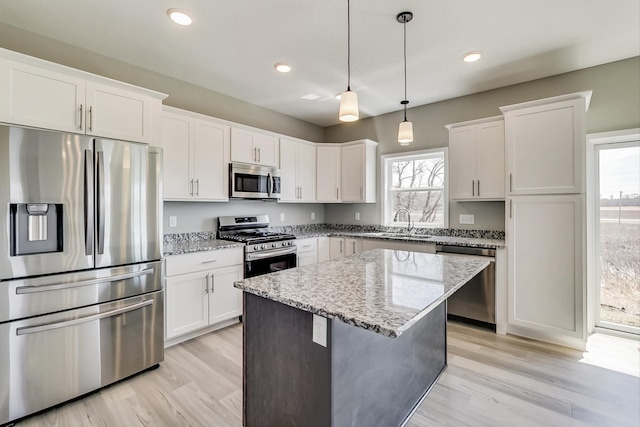 kitchen with a center island, stainless steel appliances, light wood-style floors, white cabinets, and light stone countertops