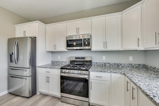 kitchen featuring light wood-style flooring, appliances with stainless steel finishes, white cabinetry, and light stone countertops