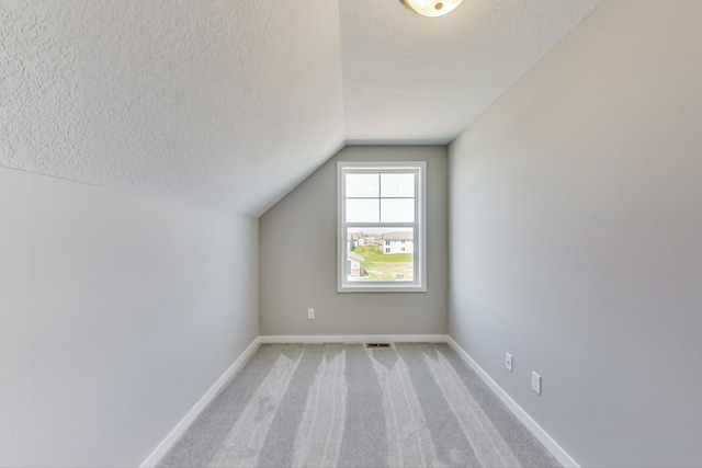 additional living space featuring visible vents, baseboards, lofted ceiling, light carpet, and a textured ceiling