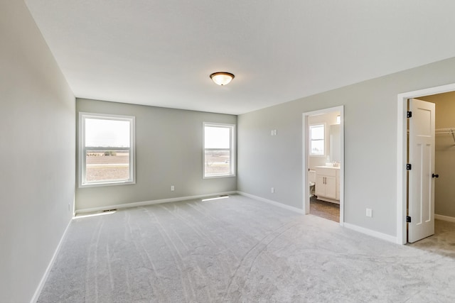 unfurnished bedroom featuring baseboards, a spacious closet, ensuite bath, and carpet flooring