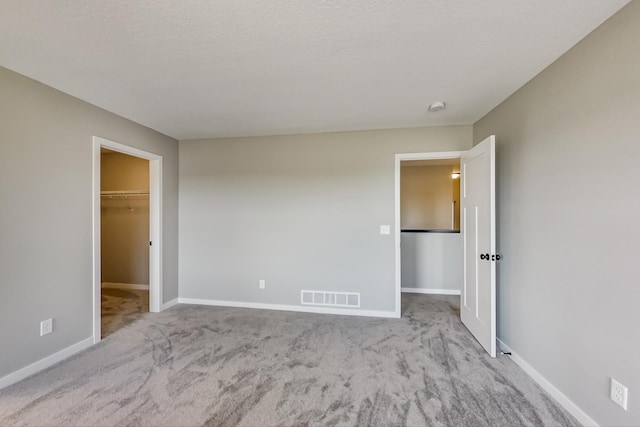 unfurnished bedroom featuring a spacious closet, visible vents, baseboards, and carpet floors