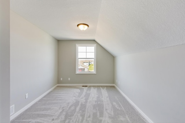 bonus room featuring visible vents, baseboards, lofted ceiling, a textured ceiling, and light colored carpet