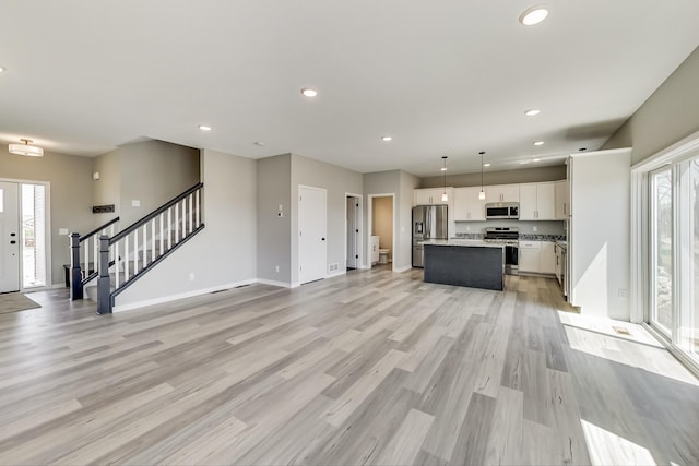 interior space with a center island, open floor plan, light wood-style floors, stainless steel appliances, and white cabinetry