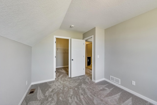unfurnished bedroom with carpet flooring, a textured ceiling, visible vents, and vaulted ceiling