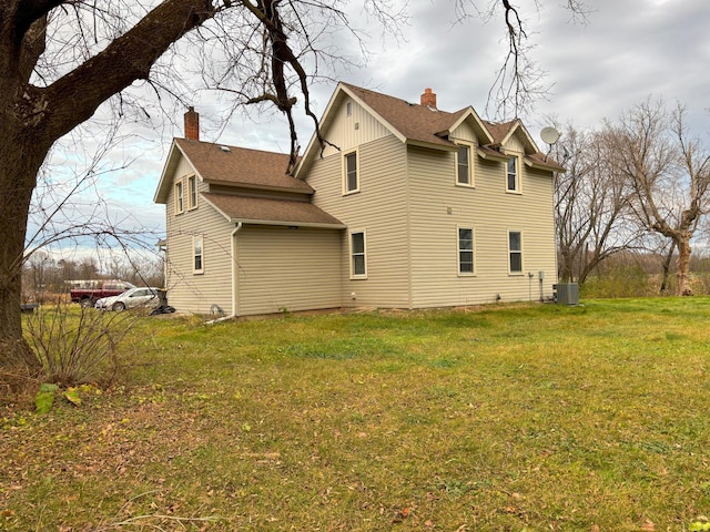 back of property featuring a yard, a chimney, cooling unit, and roof with shingles