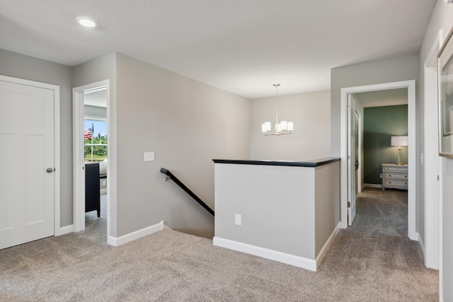 corridor with carpet floors, baseboards, a notable chandelier, and an upstairs landing