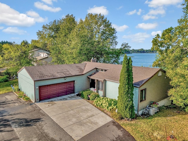 ranch-style house featuring driveway, a shingled roof, a chimney, an attached garage, and a water view