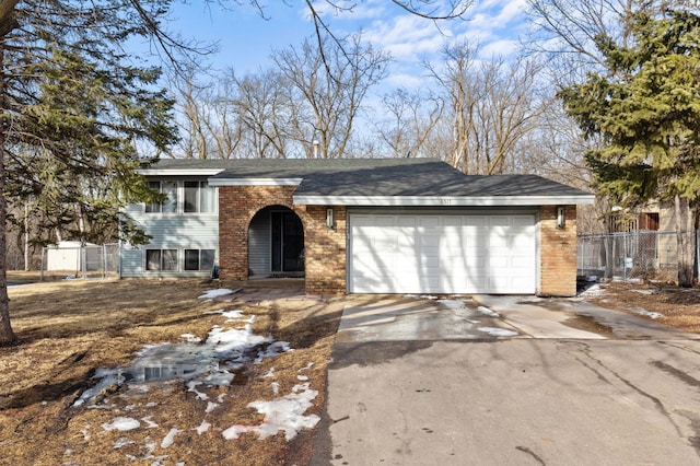 tri-level home with concrete driveway, an attached garage, fence, and brick siding