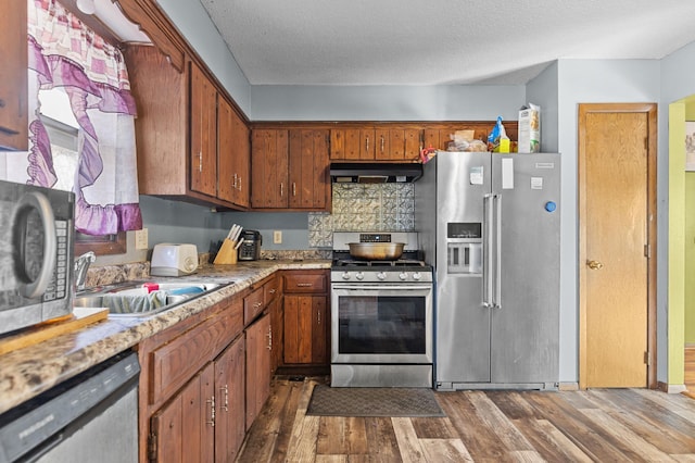 kitchen with under cabinet range hood, dark wood-style flooring, stainless steel appliances, and a sink