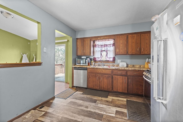 kitchen featuring stainless steel appliances, a textured ceiling, a healthy amount of sunlight, and dark wood-style flooring