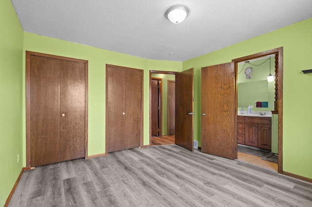 unfurnished bedroom with connected bathroom, a textured ceiling, light wood-style floors, and multiple closets