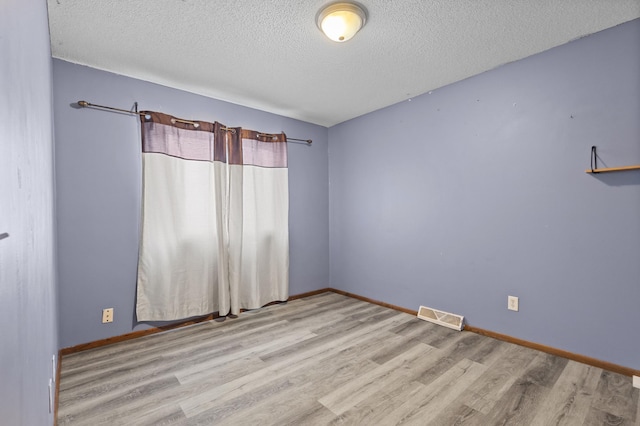 empty room featuring baseboards, wood finished floors, visible vents, and a textured ceiling