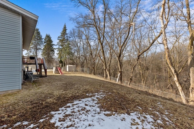 yard covered in snow featuring a deck, a playground, and fence