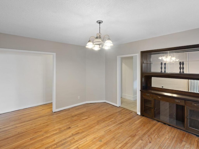 unfurnished dining area with baseboards, a textured ceiling, light wood-style flooring, and an inviting chandelier